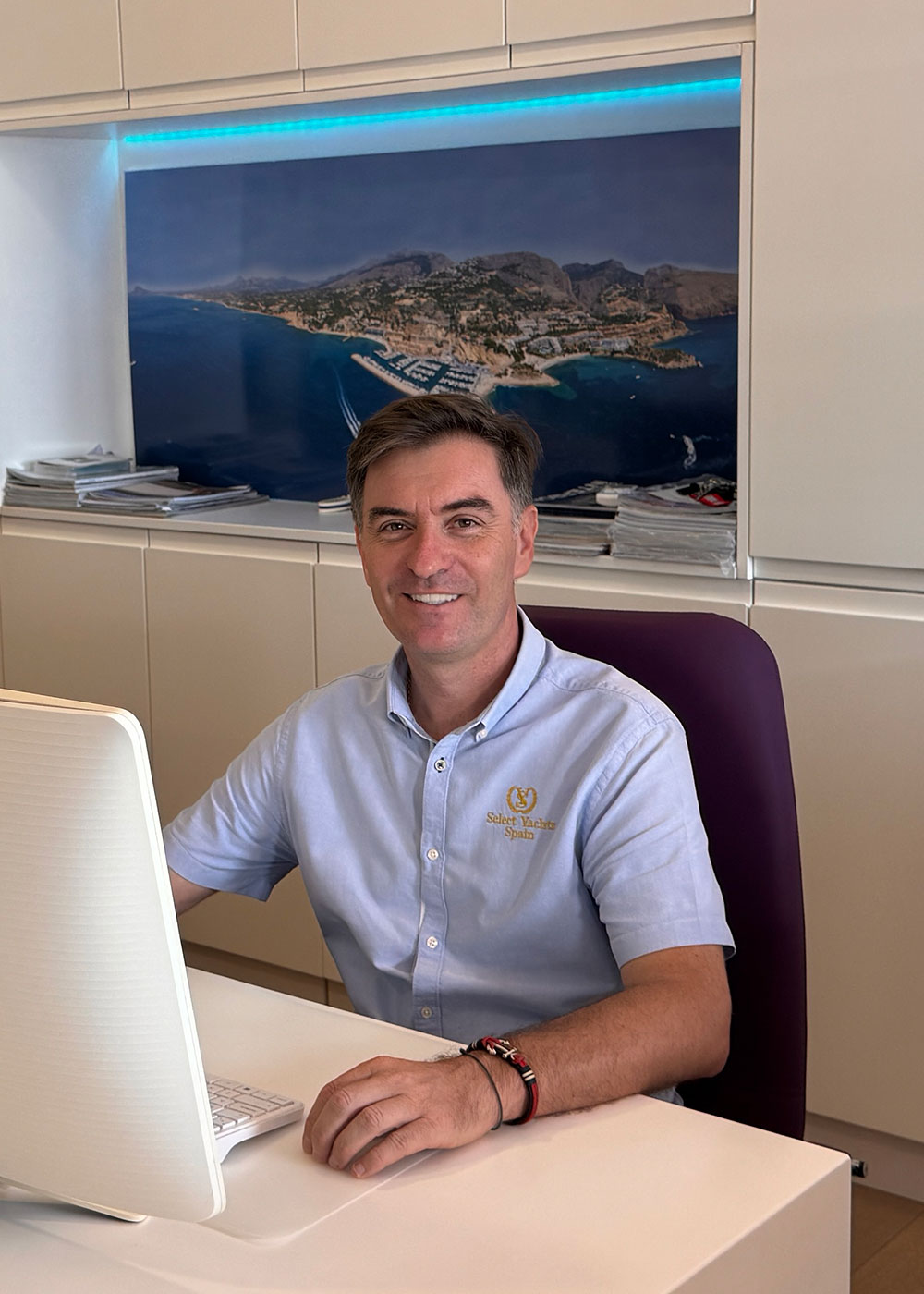 Hombre de mediana edad con camisa, sonriendo, sentado en una mesa de oficina